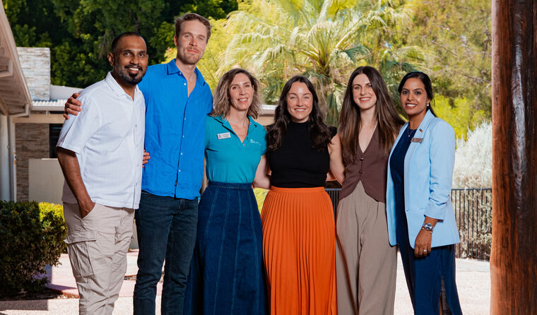 Six people stand in a row smiling at camera.