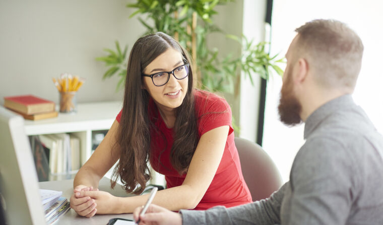 Two people talking at a desk.