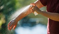 A person sprays insect repellant on their arm.