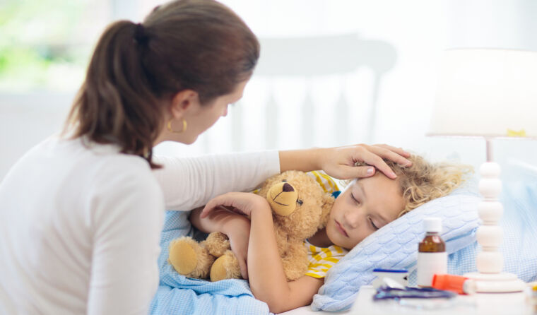 Woman with hand on an unwell young boy's forehead.
