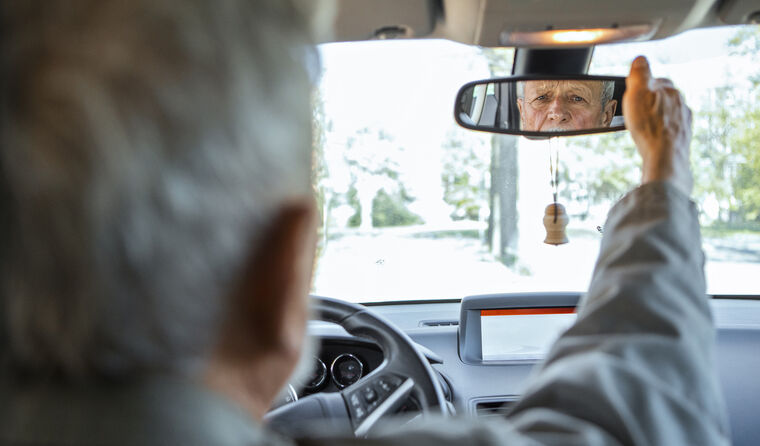 Elderly man looking in car's rearview mirror.