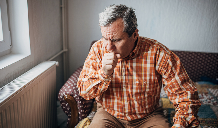 A man sitting on the couch coughing.