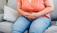 Overweight woman clutches stomach in pain.