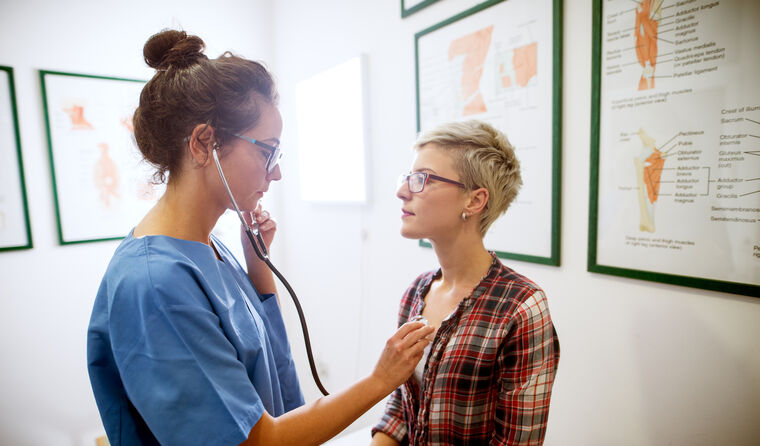 Female doctor using stethoscope on female patient.