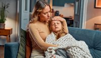 Mum with sick daughter on couch, under blanket
