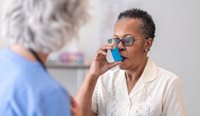 A doctor watches female patient use asthma inhaler
