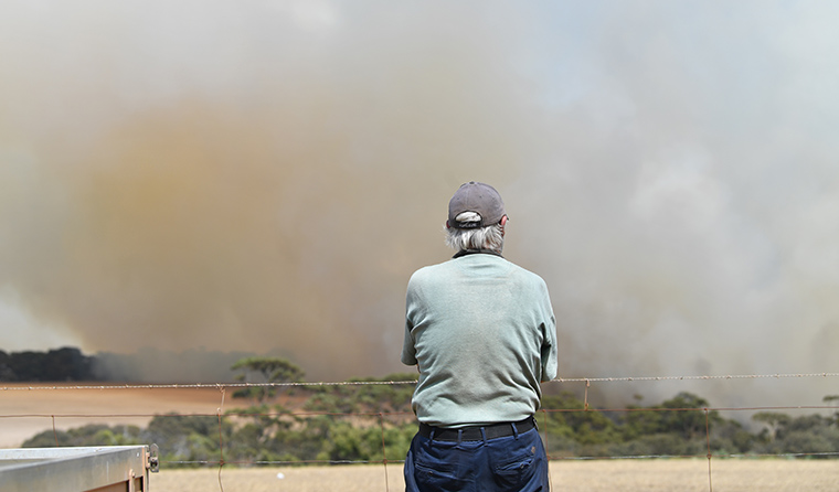 Man surveying a massive bushfire on the horizon.