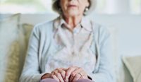 Elderly woman, slightly blurred, sits on couch.