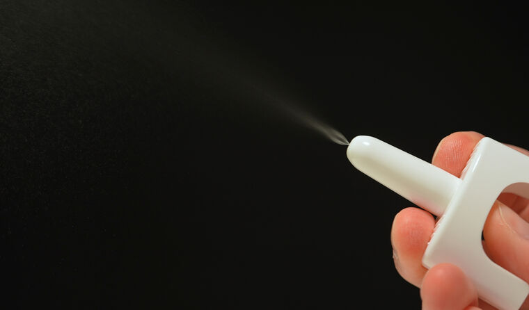 Person spraying nasal spray into mid air