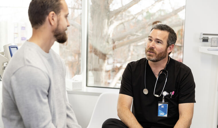 Young male doctor speaks to adult male patient.