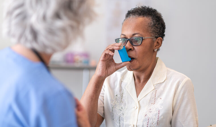 A doctor watches female patient use asthma inhaler