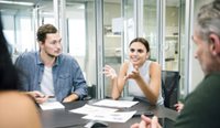 Young woman leads discussion around office table.