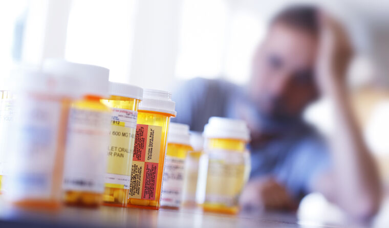 Man suffering, with opioid bottles in foreground