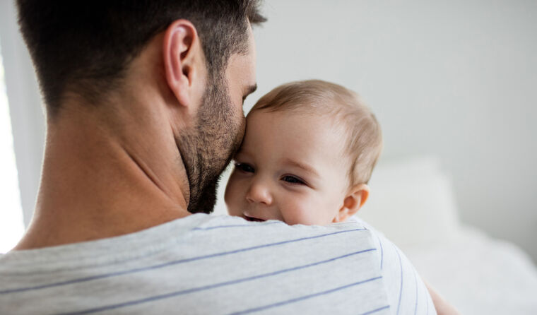 A young father holds his baby on his shoulder.