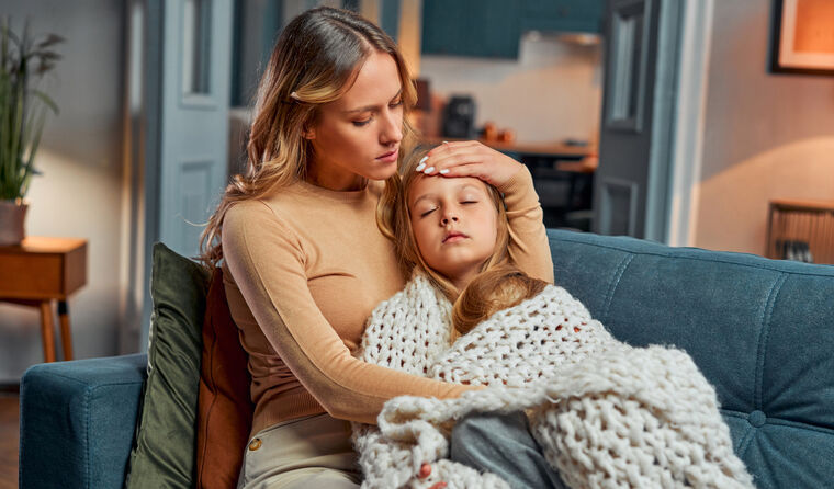 Mum with sick daughter on couch, under blanket