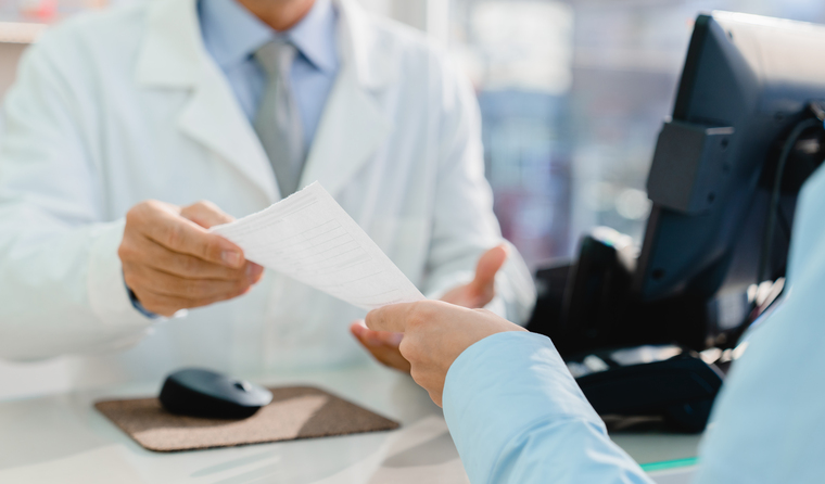 A patient handing a pharmacist a prescription.
