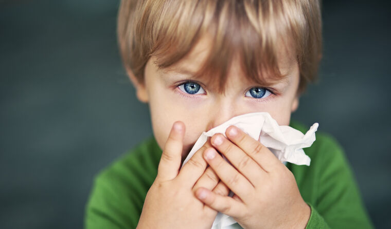 A young blue-eyed boy wipes his nose with a tissue