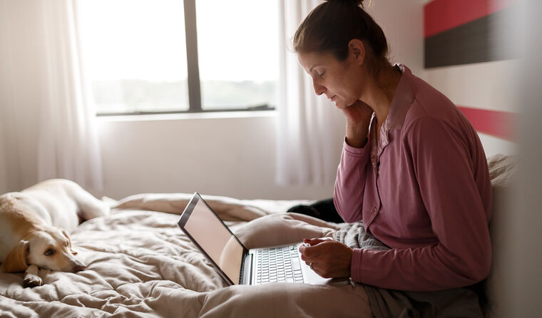 Woman sitting in bed looking at computer.