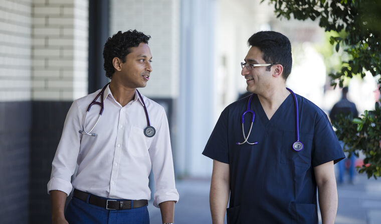 Two male doctors walking together down street.