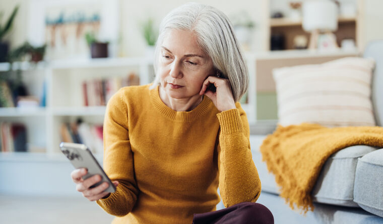 Older pensive woman sits looking at mobile phone