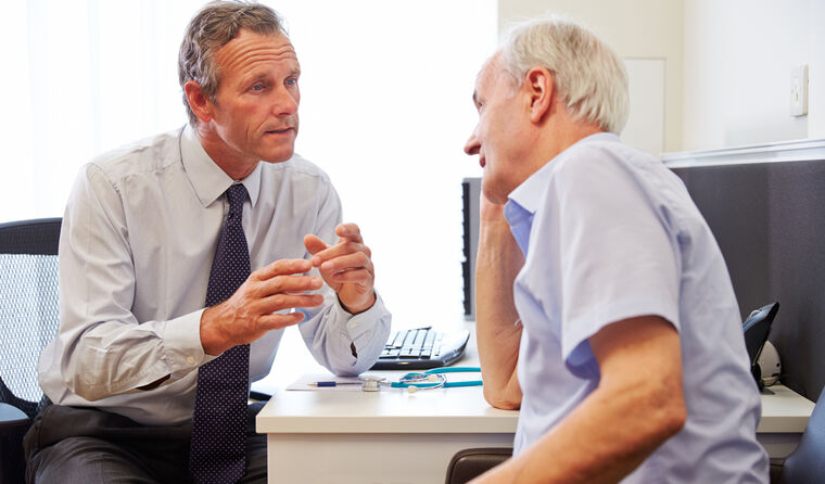 Elderly male patient sits with young male doctor.