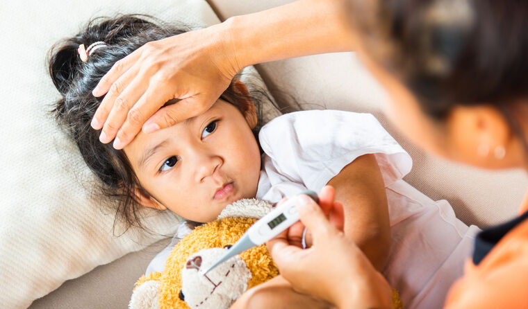 A young girl in bed, mother's hand on her forehead