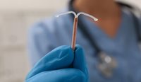 A gloved hand holds up an IUD,