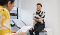Young man in striped tee sits in doctor