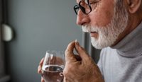 Older man takes small white pill with water