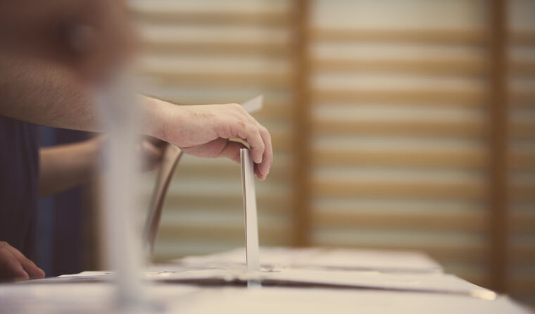A hand is seen putting a vote into a box.