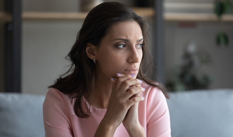 A woman with dark hair sits alone looking worried.