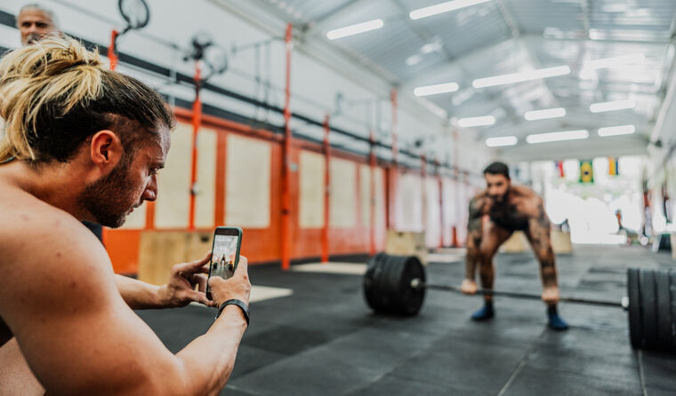Man filming another man weight lifting.