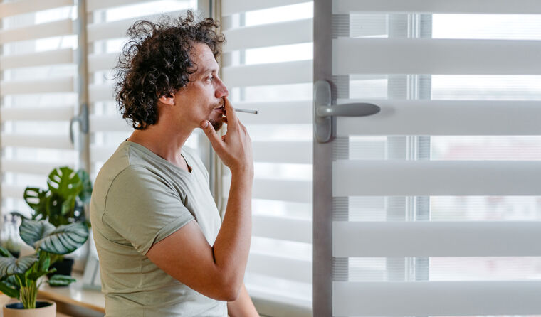 Middle-aged man smokes cigarette at window.
