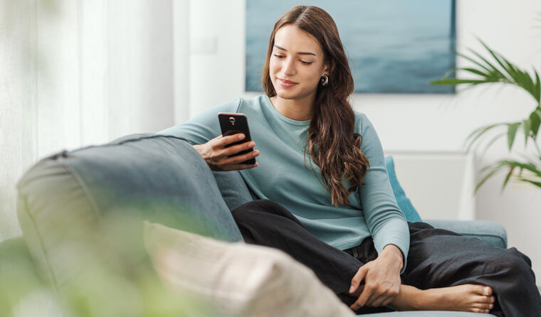 Young woman sits on couch looking at phone.