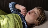 A young boy lies in bed coughing.