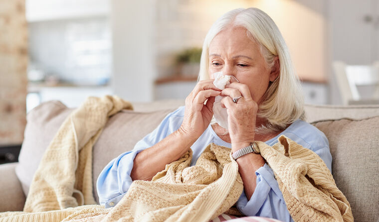 Elderly woman on couch blowing her nose.