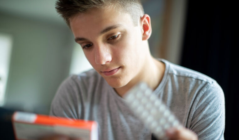 A teenage boy looks at a foil of medication