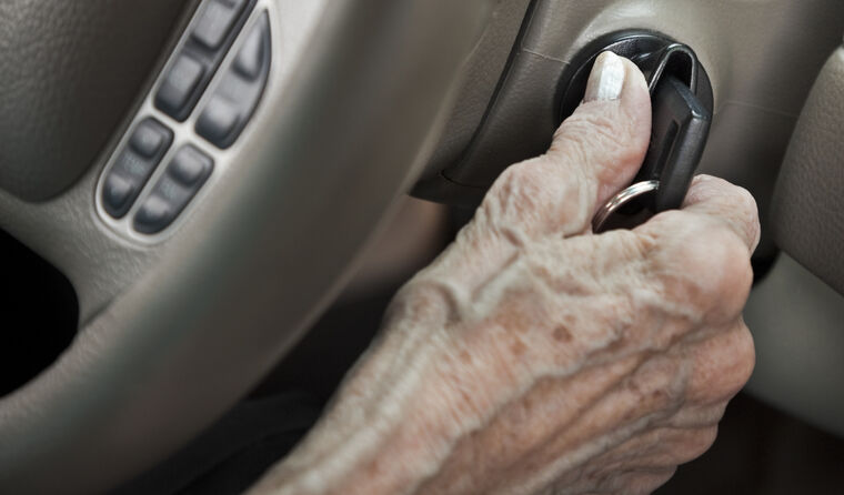 Elderly hand turning the key in a car ignition.