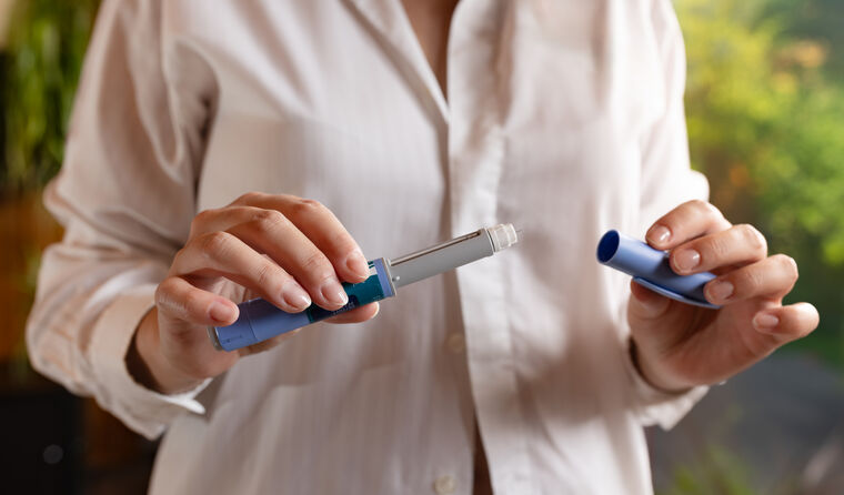 A woman holds a blue injection pen.