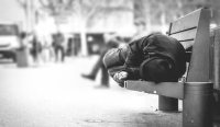 A homeless man sleeping on a park bench.