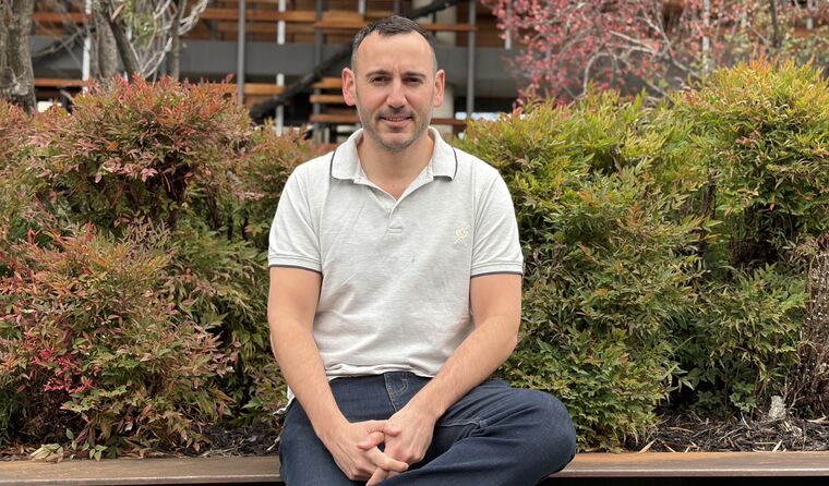 Young neat man sits outside smiling at camera.