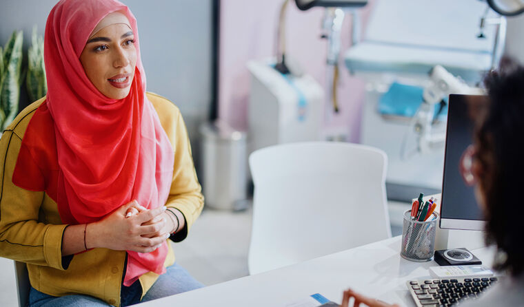 Young woman in pink hijab sits opposite doctor.