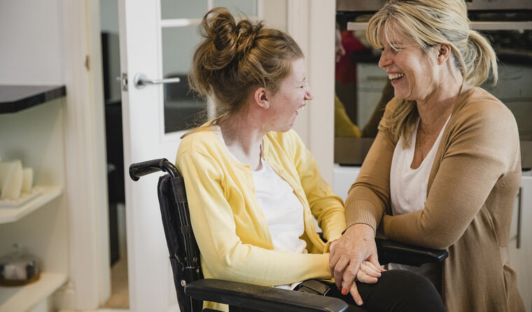 A carer and a young girl in a wheelchair laughing.