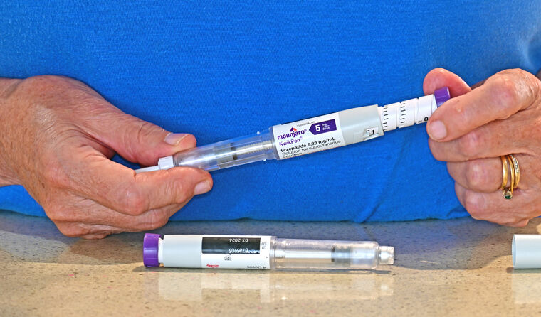 Older female hands hold a Mounjaro injectable. 
