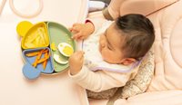 A baby sits at high chair with food, including egg