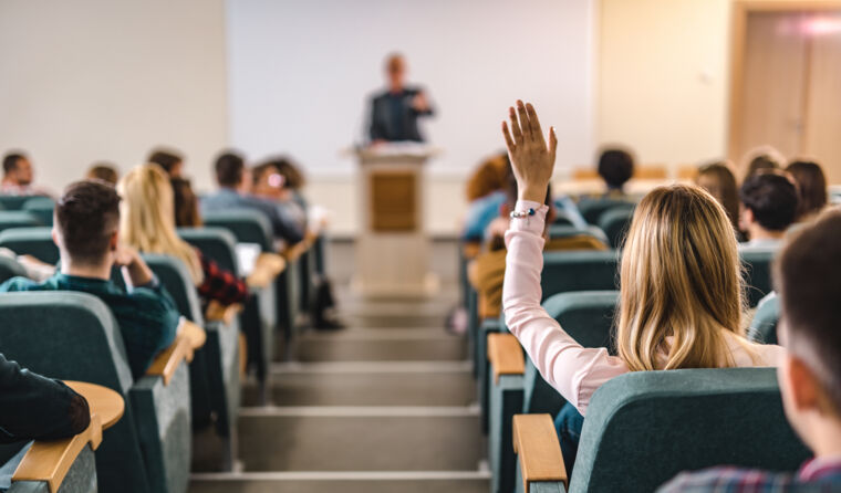 Woman in lecture theatre puts hand up to ask Q.