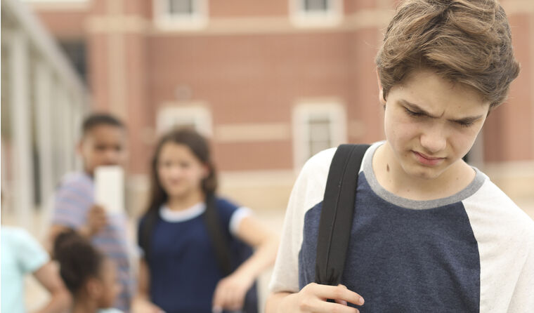  Lonely teen boy walks away from a group of kids.