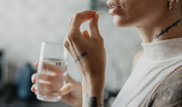 A woman about to take tablet with glass of water.