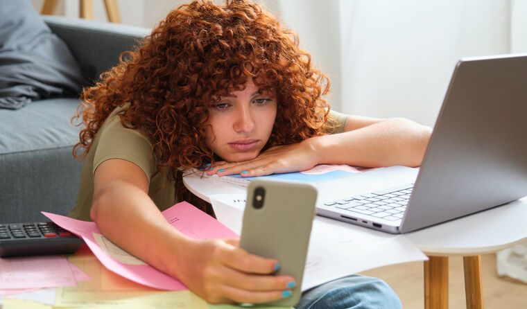 Red-haired girl on computer, distracted by phone.