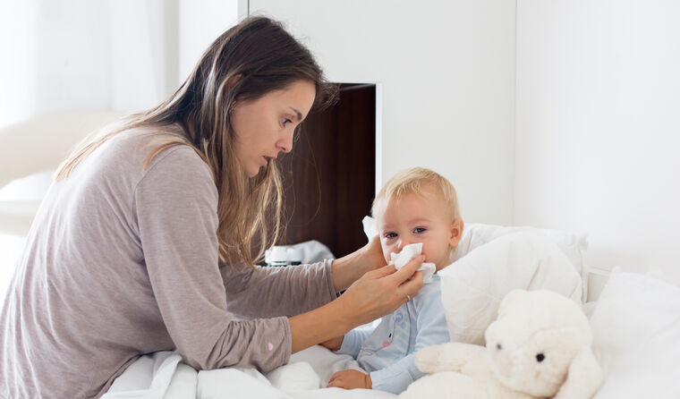 Women helping baby with the flu blow their nose.